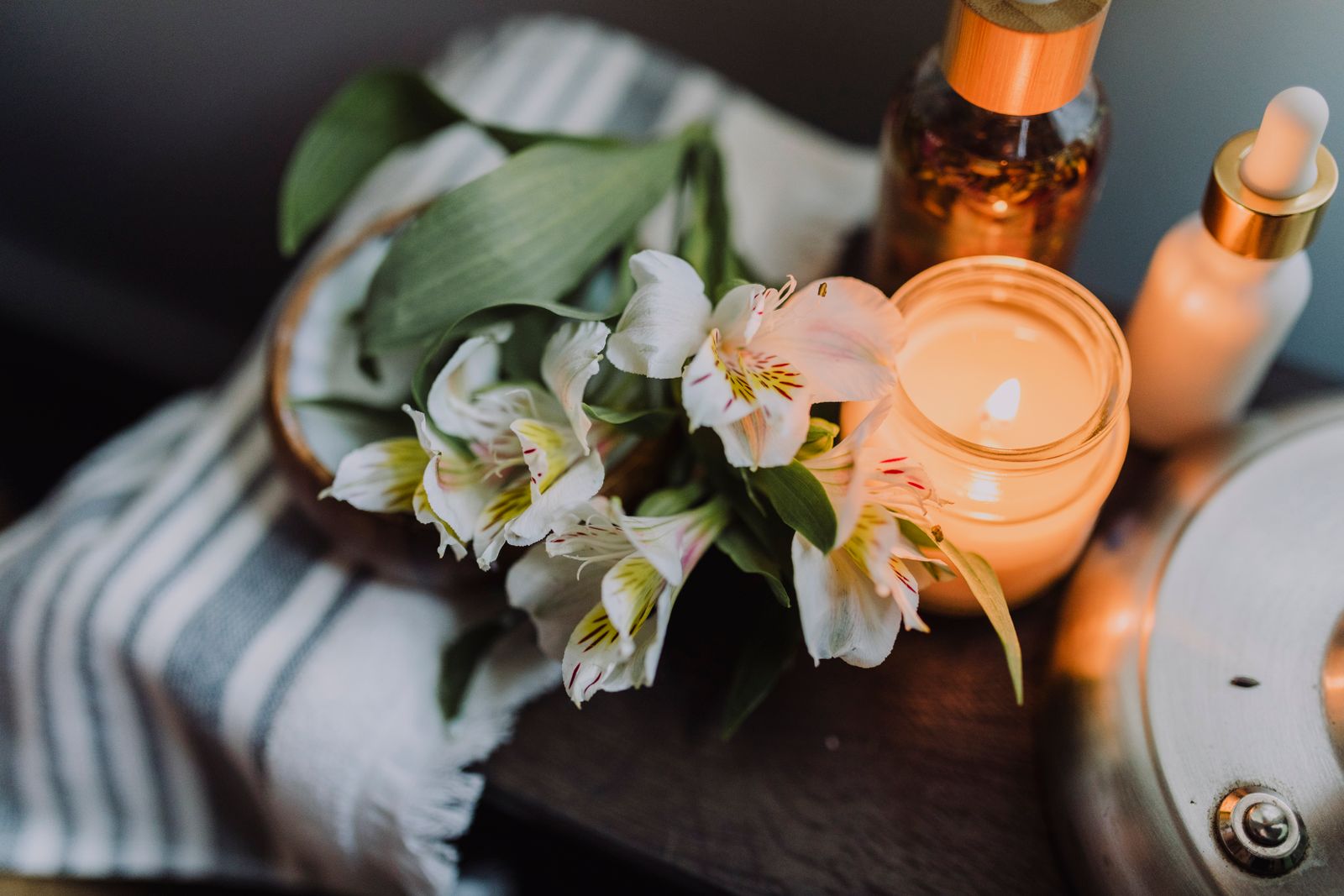 Bougie allumée dans un pot de verre, posée près de fleurs coupées sur un plateau de bois