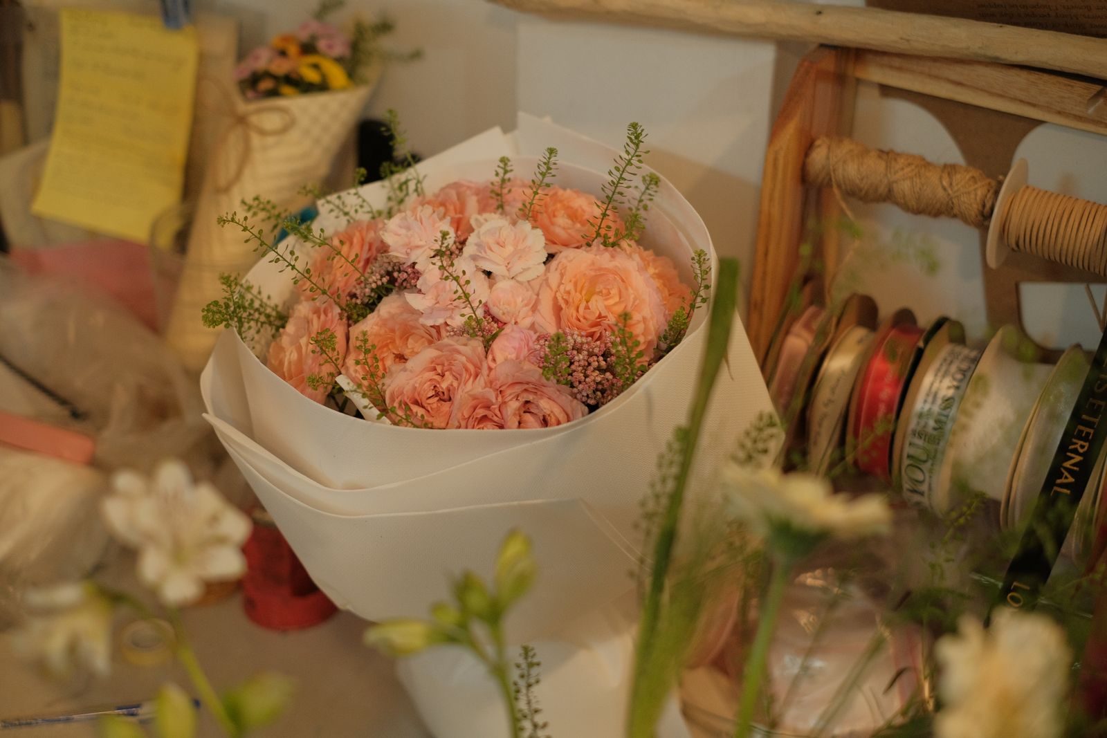 Bouquet de fleurs roses emballé dans du papier blanc, sur un plan de travail de fleuriste