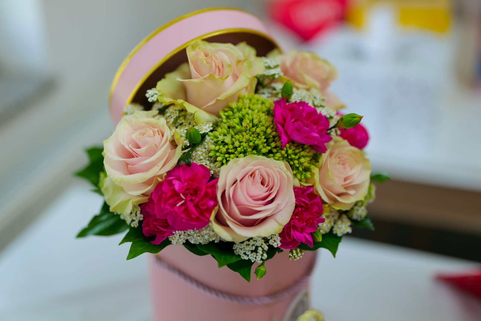 Roses pâles et œillets disposés dans une boîte ronde, composition prête à offrir